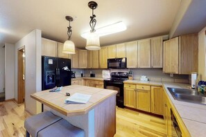 A compact kitchen with wooden cabinets, a black refrigerator, a microwave, and a small island with a bench. - Peak-view townhome with convenient central location, decks & free EV charger (Frisco)