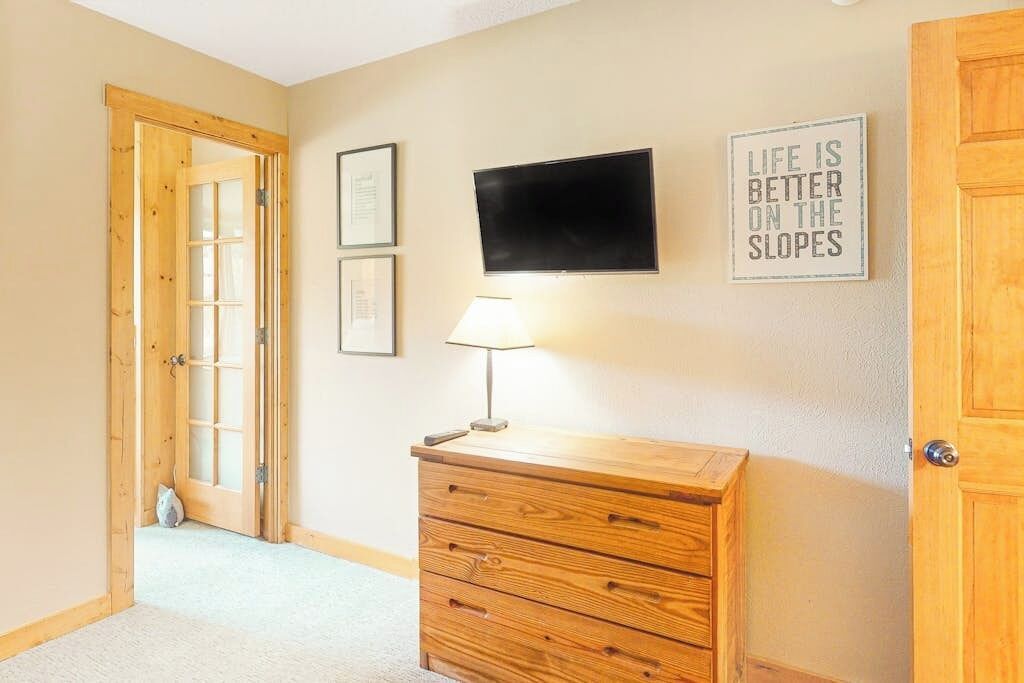 A room with a wooden dresser, a television mounted on the wall, and a door with a glass panel.