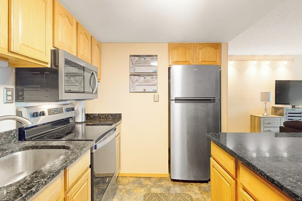 A kitchen with wooden cabinets, stainless steel appliances, granite countertops, and a tiled floor.