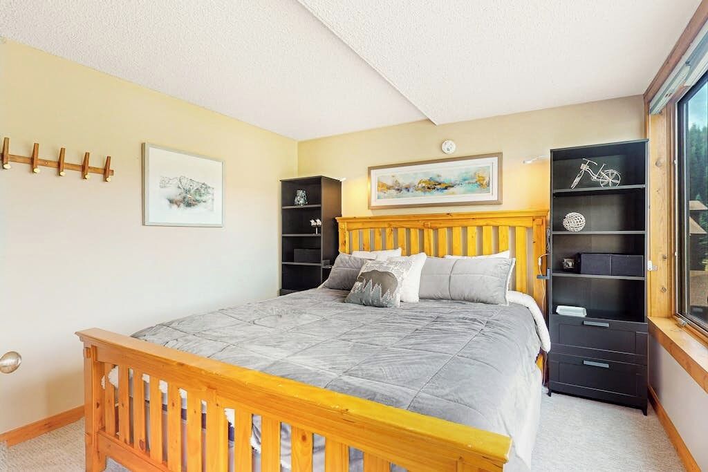 A bedroom with a bed, wooden headboard, bedside tables, a wardrobe, and a window.