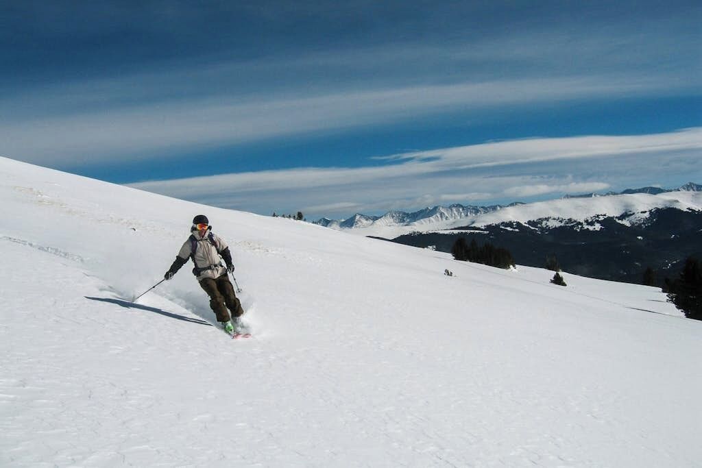 A person skiing down a snow-covered slope with mountains in the background.