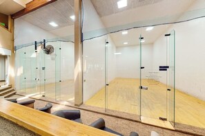 Ein Squashplatz mit Glaswänden, Holzboden und einer Sitzgelegenheit mit Stühlen.