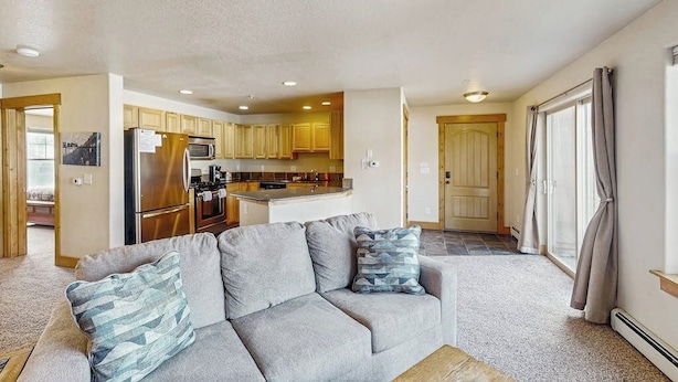 A modern living room with a sofa, a kitchen in the background, and a sliding glass door leading to a balcony. - Convenient Mountain Condo w/Free WiFi, Mtn Views, Private Washer/Dryer, & Cable (Fraser)