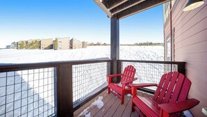Una terraza de madera con sillas rojas, barandilla metálica y vistas a un paisaje nevado.