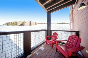 A wooden deck with red chairs, a metal railing, and a view of a snowy landscape. - Ideally located mountain getaway w/ shared pool, gas grill, & scenic balcony (Granby)