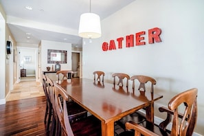 A dining area with a wooden table and chairs, a 'GATHER' sign on the wall, and a hallway leading to another room. - Ideally located mountain getaway w/ shared pool, gas grill, & scenic balcony (Granby)