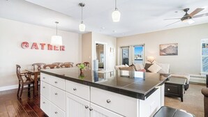 Una cocina moderna con una isla central, sillas de madera, una mesa de comedor y un área de estar con un sofá y una mesa de centro.