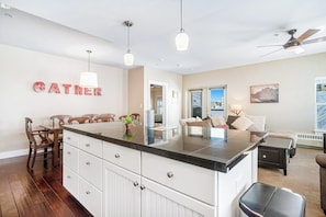 A modern kitchen with a central island, wooden chairs, a dining table, and a living area with a sofa and a coffee table. - Ideally located mountain getaway w/ shared pool, gas grill, & scenic balcony (Granby)