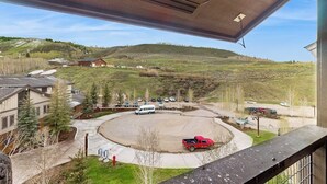 Vista des d'un balcó sobre un aparcament amb una camioneta vermella, edificis i un paisatge amb turons.