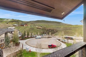 Blick vom Balkon auf einen Parkplatz mit einem roten LKW, Gebäuden und einer hügeligen Landschaft.