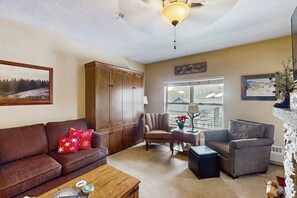 Ein Wohnzimmer mit braunem Sofa, einem Holzkasten, einem Sessel, einem Tisch mit Lampe und einem Kamin.
