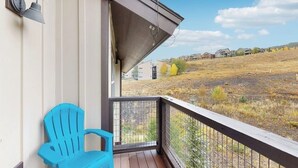 En balkon med en blå stol, gelænder i metal og udsigt over en græsplæne med bygninger i det fjerne.