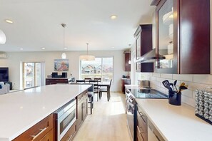 A modern kitchen with an island, dark wooden cabinets, and a dining area with a view. - Gorgeous mountain home with deck, pool table, fast WiFi & fireplace - near town (Tabernash)