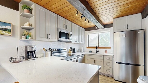 Una cucina moderna con mobili bianchi, elettrodomestici in acciaio inossidabile e soffitto in legno.