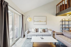 Ein Wohnzimmer mit Sofa, Couchtisch, Lampe und einem Gemälde an der Wand.