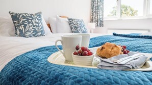 Una cama bien hecha con un edredón azul, una bandeja con una taza, uvas y un pastel.