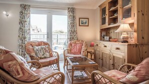 Un salón acogedor con muebles de mimbre, una mesa de centro de vidrio y un mueble de madera con estantes.