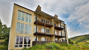 Un edificio a più piani con balconi, ampie finestre e uno sfondo collinare.