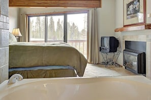 Ein Schlafzimmer mit großem Fenster, Kamin, Fernseher und Badewanne.