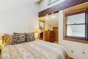 Ein Schlafzimmer mit einem Bett, gestreiften Kissen, einem Nachttisch, einer Lampe, einem Kleiderschrank und einem Fenster mit Aussicht.