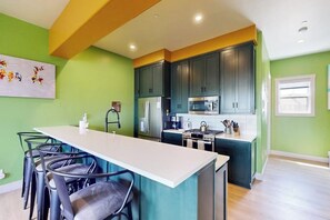 A modern kitchen with dark cabinets, a central island with bar stools, and a bright green wall. - Charming townhome in central locale with fireplace & balcony - dog-friendly (Granby)