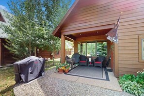 Eine überdachte Terrasse mit Gartenmöbeln, einem Grill und Kübelpflanzen.