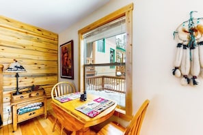Ein gemütliches Zimmer mit einer Holzwand, einem Esstisch mit Stühlen, einem Fenster mit Blick auf ein Gebäude und einem Traumfänger an der Wand.