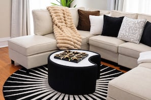A modern living room with a sectional sofa, a round coffee table with a geometric pattern, and a black and white striped rug.