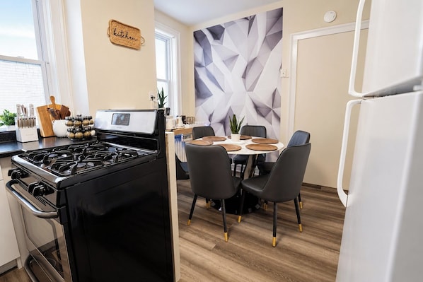 A modern kitchen with a gas stove, a dining table with chairs, and a decorative wall.