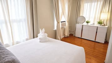 A hotel room with a neatly made bed, a dresser with a mirror, and a bedside table with a lamp.