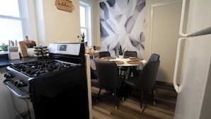 A modern kitchen with a gas stove, dining table, chairs, and a decorative wall. - 6BR Apt • Workspace • Near Lakefront + Red Line (Chicago)