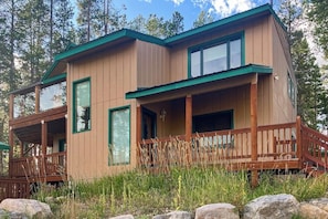 Eine zweigeschossige Holzhütte mit Balkon, großen Fenstern und einer Veranda.