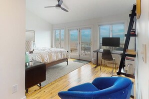 Ein Schlafzimmer mit Bett, Schreibtisch, Stuhl, Fernseher und Balkon.