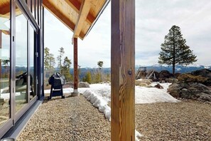 A modern building with large glass windows, a wooden deck, and a view of snow-covered ground and distant mountains. - Modern off grid cabin with stocked kitchen & private mountain view- dog friendly (Tabernash)