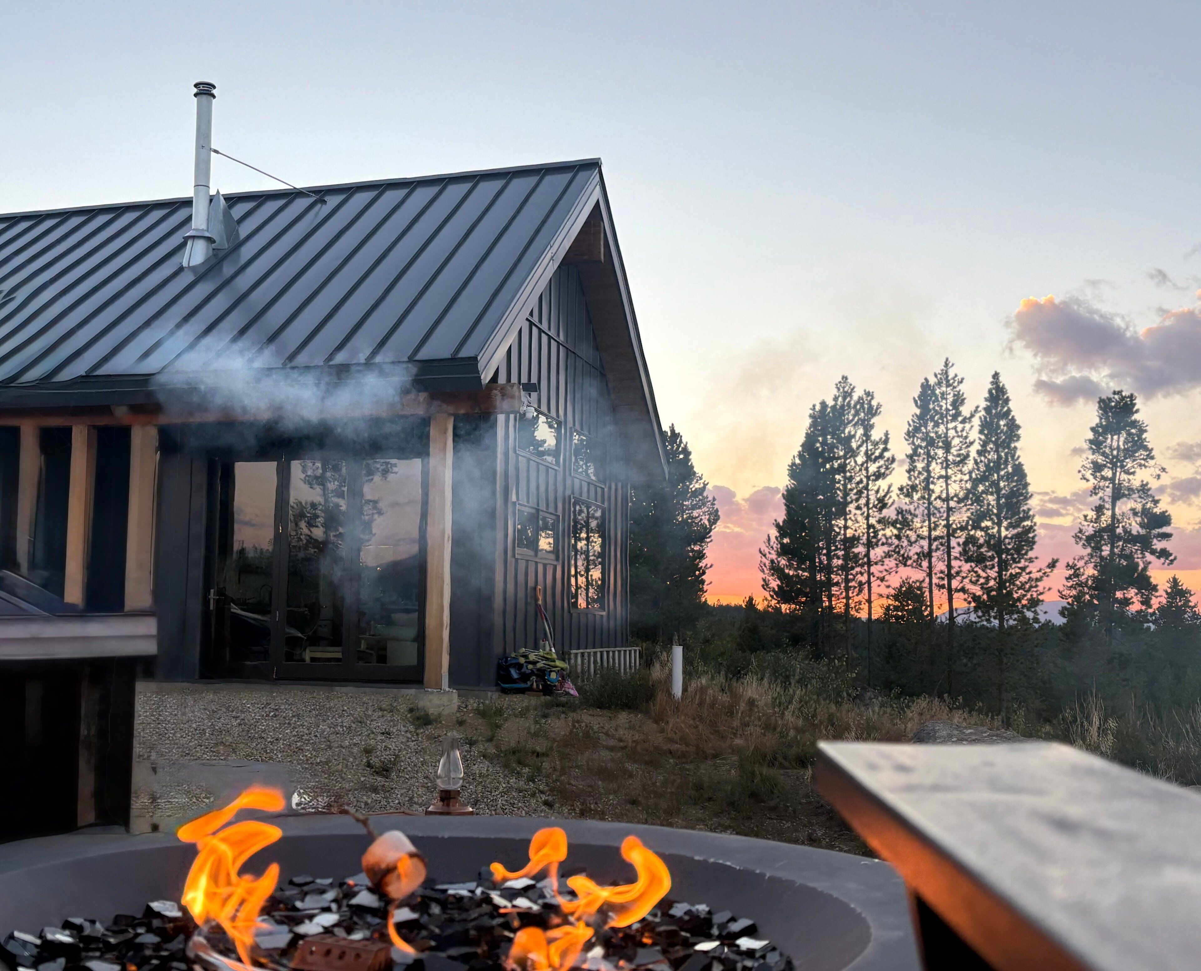 A modern house with a metal roof, a chimney, and a fire pit with flames.
