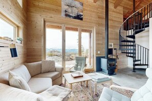 A cozy cabin interior with a sofa, armchairs, a table, a fireplace, and a spiral staircase. - Modern off grid cabin with stocked kitchen & private mountain view- dog friendly (Tabernash)