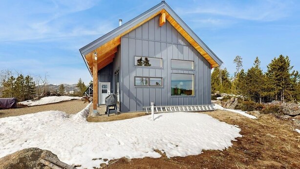 Una casa moderna con techo inclinado, un porche de madera y vistas del paisaje circundante.