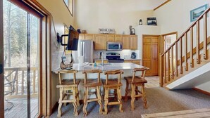 A kitchen with wooden cabinets, a large island with bar stools, a refrigerator, microwave, and a sign that says 'GRAND LAKE'.