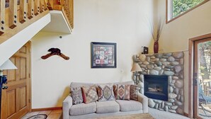 A living room with a stone fireplace, a sofa with patterned cushions, a wooden coffee table, and a framed picture on the wall.