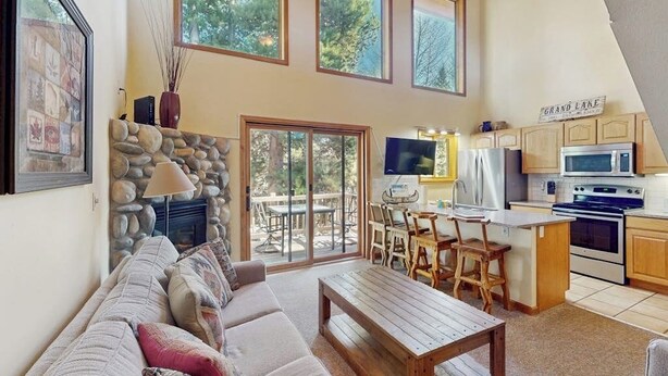 A spacious living area with a stone fireplace, a wooden dining table, and a kitchen with wooden cabinets and a large window.