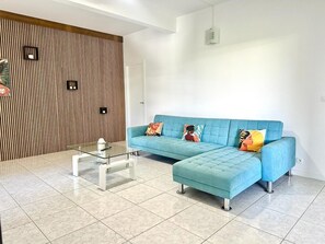 A modern living room with a blue sofa, a glass coffee table, and a wooden accent wall.