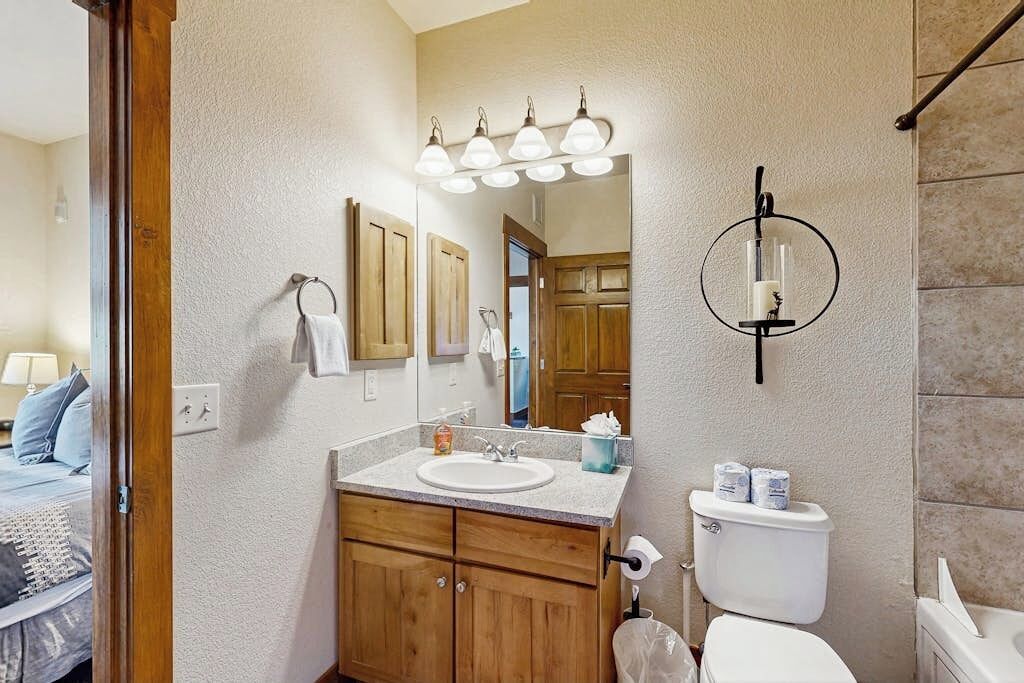 A bathroom with a wooden vanity, a sink, a toilet, and a mirror with lights.
