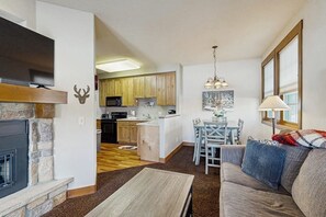 Ein Wohnzimmer mit Kamin, einer Couch, einem Esstisch und einer Küche im Hintergrund.