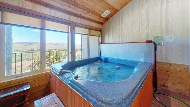 Een houten interieur met een jacuzzi, grote ramen en uitzicht op het platteland.