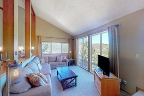 A living room with a sofa, coffee table, TV, and large windows.