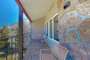 A covered porch with stone walls, wooden railing, and wicker chairs.