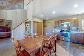 A dining area with a wooden table and chairs, a kitchen with wooden cabinets and stainless steel appliances, and a staircase leading to another level.