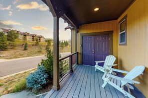 Eine Veranda mit Holzgeländer, einer violetten Tür und zwei weißen Adirondack-Stühlen.