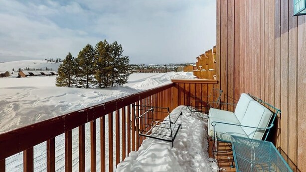 A wooden balcony with a metal chair and a metal table, overlooking a snowy landscape with trees and a clear sky. - Spacious townhome with a scenic deck, grill & washer/dryer - near the lake (Grand Lake)