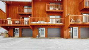 A multi-story wooden building with balconies, garage doors, and a snow-covered ground. - Spacious townhome with a scenic deck, grill & washer/dryer - near the lake (Grand Lake)